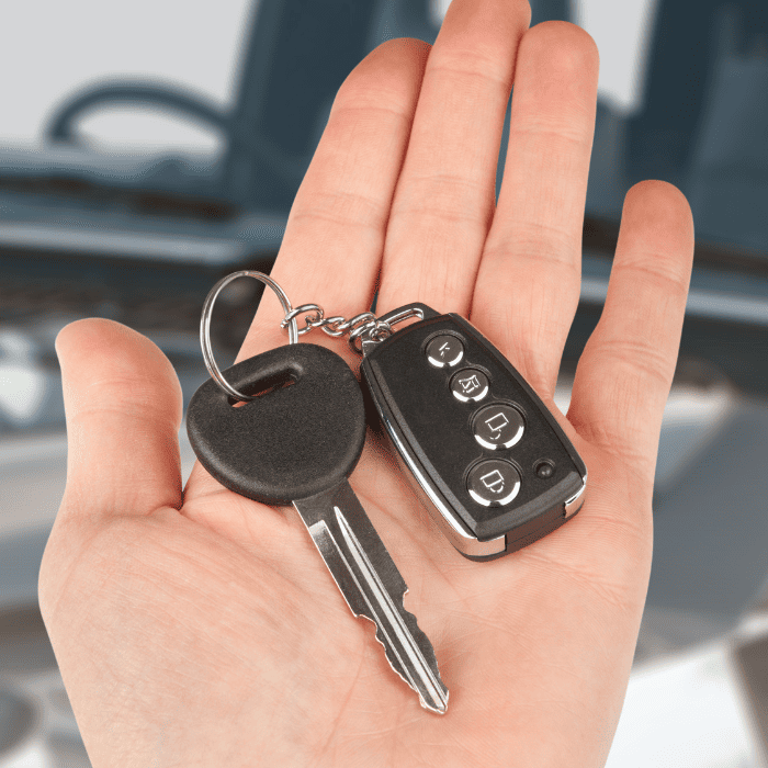 A hand holds a car key and a key fob with buttons, poised in front of a blurred car interior, channeling the precision of a skilled locksmith in Jurupa Valley.