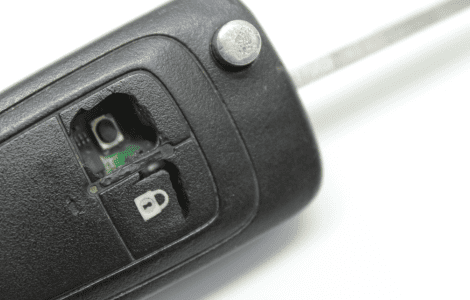 A close-up of a car key with damaged rubber buttons, exposing the internal circuit beneath the lock and unlock symbols—perfect for a Locksmith Beaumont to repair.