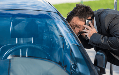 A man in a suit talks on the phone while looking through the window of his parked car, possibly waiting for a Locksmith Redlands to arrive.