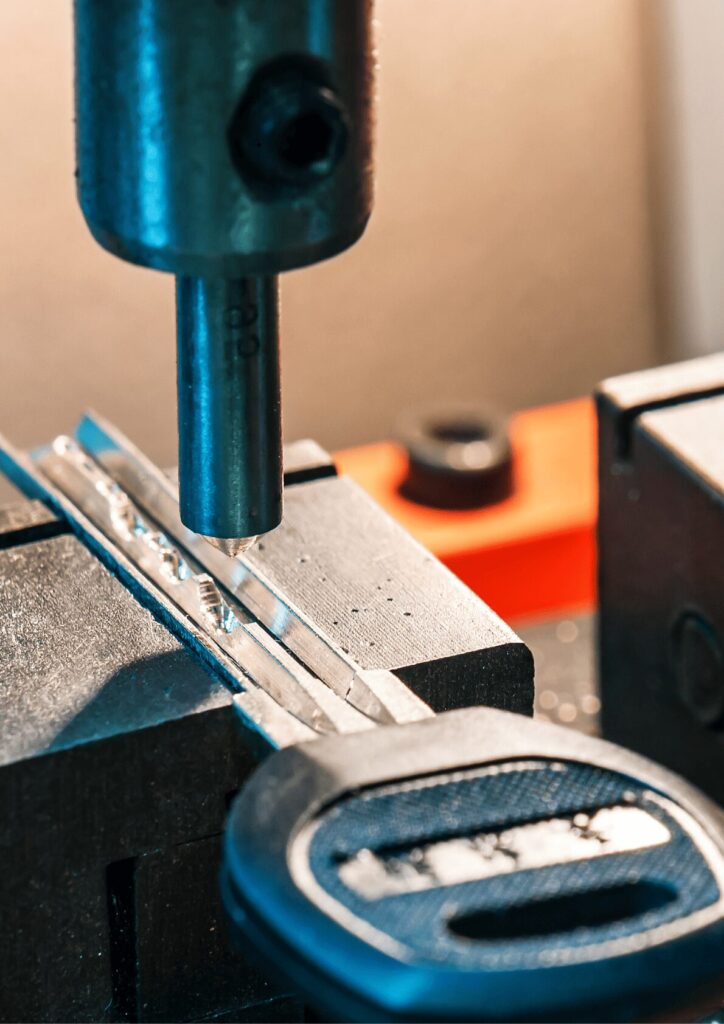A key cutting machine in operation, with a blank key clamped in place as the machine carves grooves into the metal for precise car key replacement.
