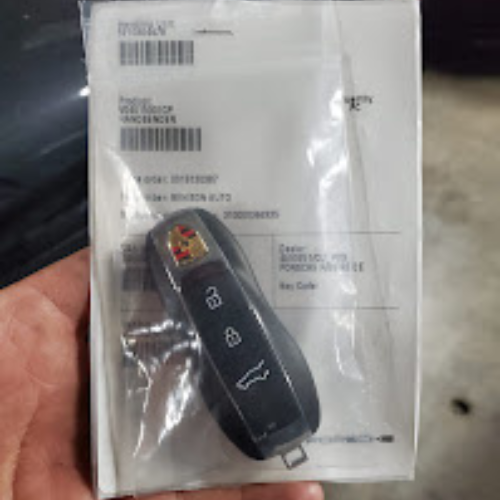 A car key fob is placed on top of a clear plastic bag containing paperwork with barcodes and printed text.